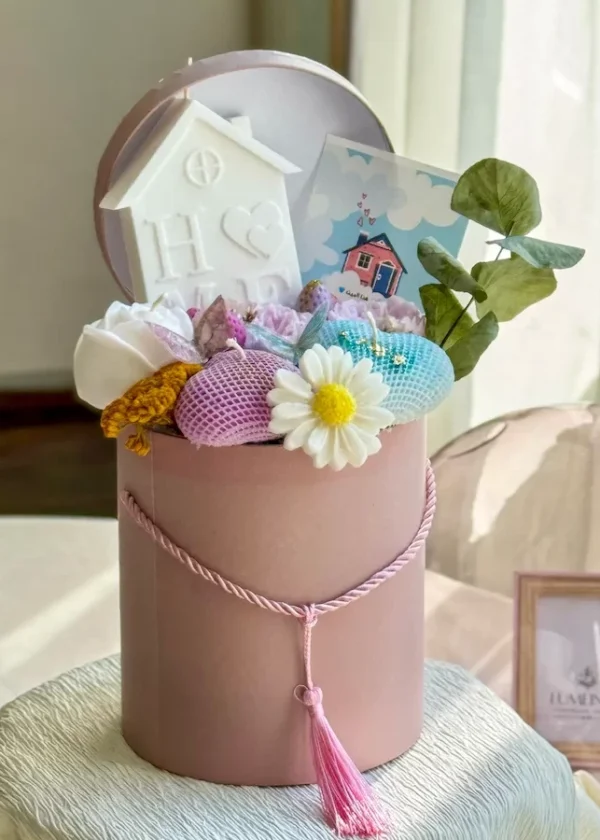 Handmade candle gift box featuring wax flowers, a house-shaped candle, and assorted decorative blooms.