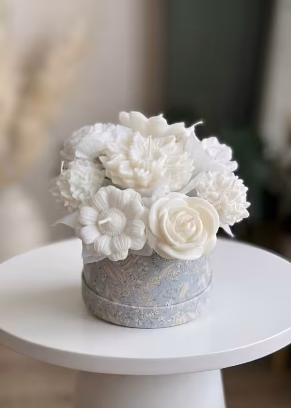 Handmade white flower-shaped candle bouquet in a decorative blue gift box, featuring roses, dahlias, and ranunculus candles arranged as a floral centerpiece