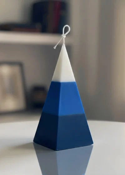 A luxury free-standing pyramid candle by Lumeinas featuring three smooth color-blocked layers of white, royal blue, and dark navy blue on a reflective white surface.