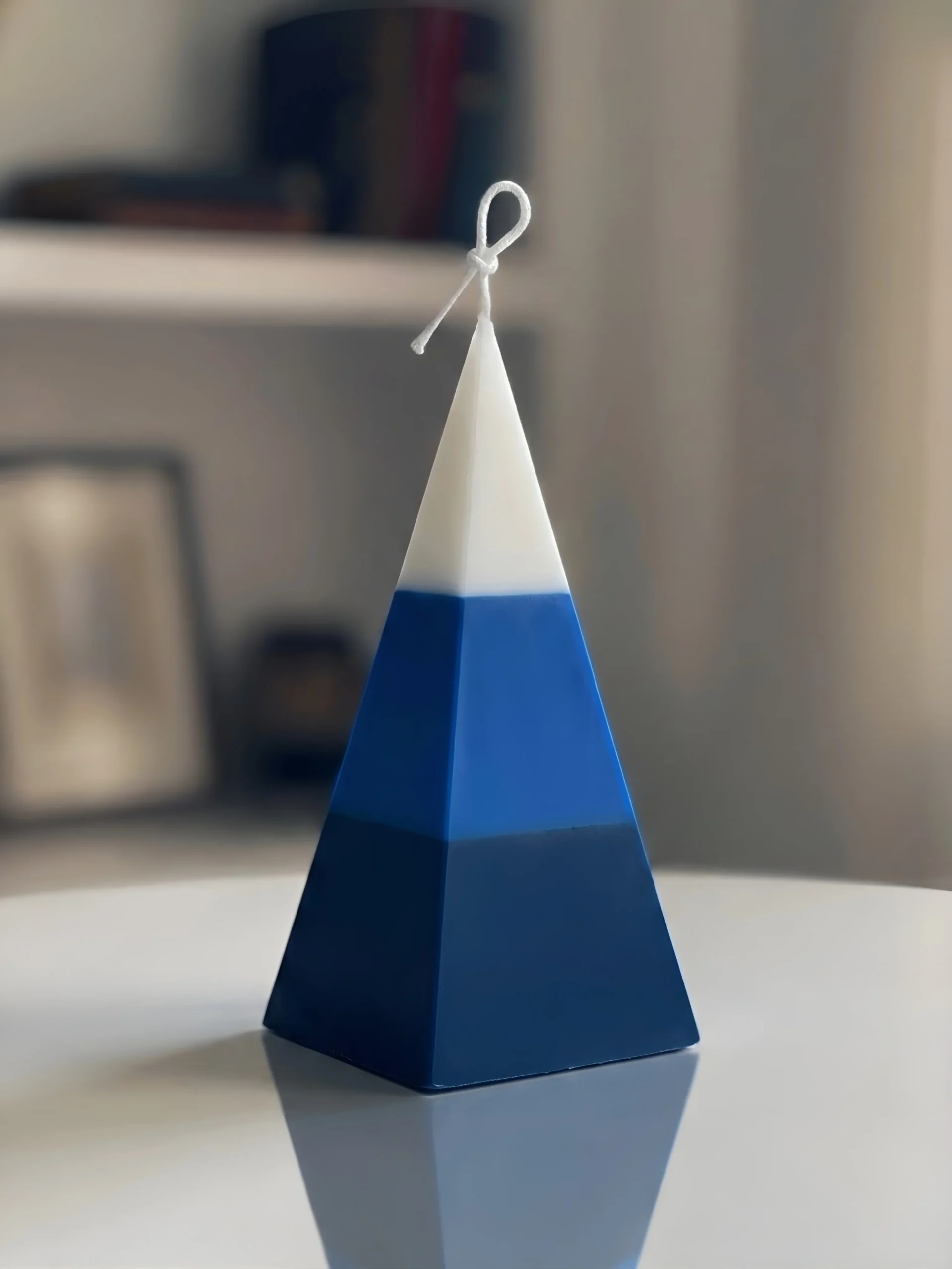 A luxury free-standing pyramid candle by Lumeinas featuring three smooth color-blocked layers of white, royal blue, and dark navy blue on a reflective white surface.